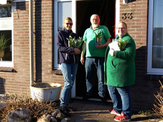 Drie mensen voor een huisdeur met een plantje in de handen